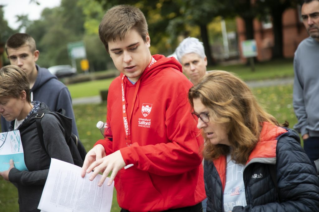 Photo of a volunteer wearing a University of Salford red hoodie guiding people