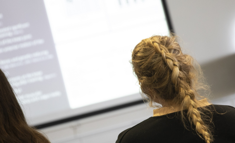 Three students are listening to a presentation and watching a slide show.